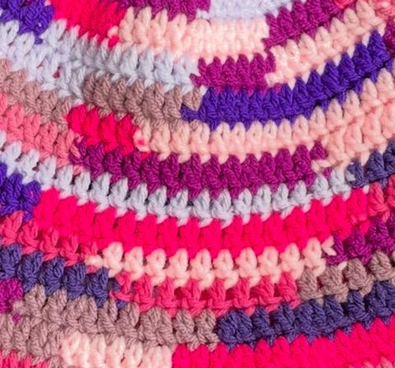 May include: A multi-colored crochet fabric featuring a dense, textured pattern of interlocking yarn loops. The design displays a vibrant mix of hot pink, deep purple, light lavender, soft peach, and muted taupe colors arranged in horizontal rows.