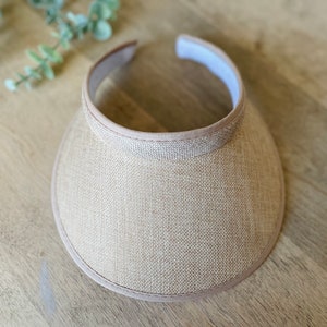 May include: A beige sun visor with a woven texture and a light brown trim around the edge.