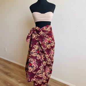 May include: A maroon wrap skirt with a gold and red floral pattern. The skirt is tied at the waist and falls to the ankles.