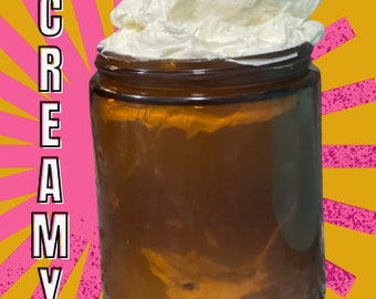 May include: A glass jar filled with a thick, white, creamy substance. The jar has a brown lid and is sitting on a yellow and pink background. The text "SOOO CREAMY!" is written in pink letters on the left side of the image.