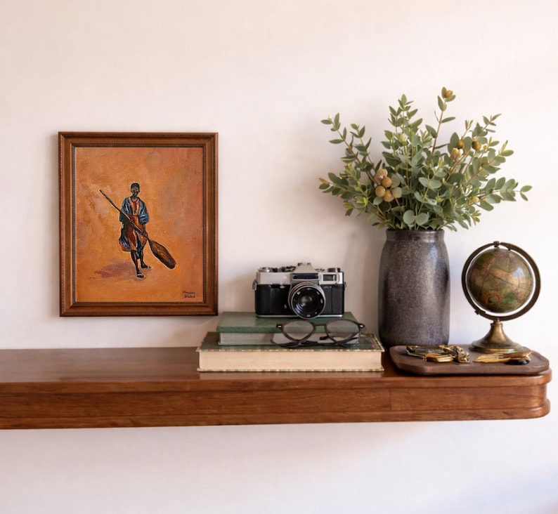 May include: A wooden shelf displays a framed painting, a vintage camera, books, glasses, a vase with greenery, and a globe. The painting depicts a figure holding a broom. The camera is black and silver.