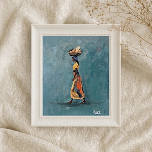 May include: A framed oil painting on a textured background depicts a person walking in profile against a teal backdrop. The person wears a yellow and orange patterned garment and carries a basket of produce on their head. The signature is visible.