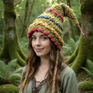 Puede incluir: Un sombrero de ganchillo hecho a mano, verde oliva, con una parte superior puntiaguda y acentos coloridos. El sombrero presenta rayas rosas, azules y amarillas y una borla trenzada a juego. Un accesorio caprichoso, perfecto para disfraces o uso diario.