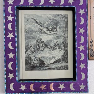 May include: A rectangular purple picture frame decorated with silver star and crescent moon cutouts. The frame features a border of small iridescent beads and contains a black and white historical print depicting figures around a map.