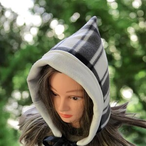 Puede incluir: Un gorro con capucha puntiaguda con un patrón de cuadros en blanco y negro. La capucha está forrada con una tela suave de color blanco roto. Una cinta negra está atada en la base de la capucha. El gorro está diseñado para brindar calidez y estilo.