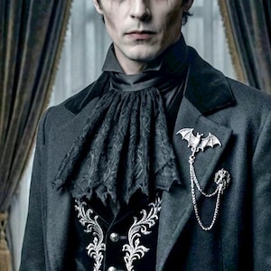 May include: A dark gray coat with a black velvet collar and a black lace ascot. A silver bat brooch with a chain is pinned to the coat. The vest underneath is black with silver embroidery.