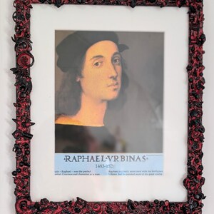 May include: A framed portrait of Raphael wearing a black cap and shirt, with text reading RAPHAEL VRBINAS 1483-1520. The frame features a textured, raised relief design in black and red, composed of various small, intricate, and abstract shapes.