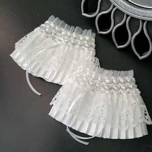 May include: Two white lace wrist cuffs with pleated fabric and satin ribbon ties.