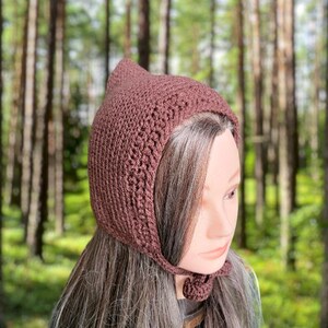 Puede incluir: Un gorro de punto de ganchillo marrón con la parte superior puntiaguda y una lazada. El gorro está hecho con un patrón de punto sencillo y tiene una sensación suave y acogedora.