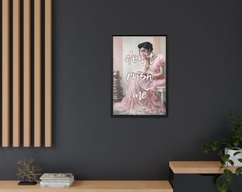 May include: Framed art print featuring a woman in a pink dress with the text "don't rush me". The artwork is set against a soft, blurred background, with a stack of books visible. The frame is black.