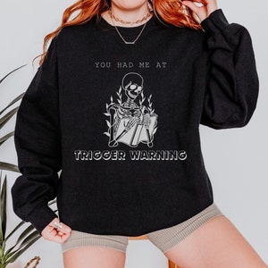 May include: Black sweatshirt with a white skeleton reading a book and the text "You had me at trigger warning".