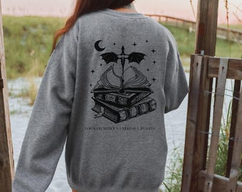 Può includere: Una felpa grigia con una grafica nera di un drago appollaiato su una pila di libri. Il testo "A dragon without a book is a tragedy" è stampato sotto la grafica.