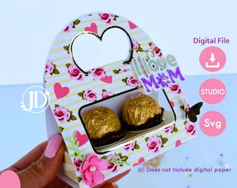 May include: A printable template for a Mother's Day gift box. The box is decorated with pink and white roses, hearts, and stripes. The box has a heart-shaped cutout on the top and a window on the front to display treats. The text "I love Mum" is on the front of the box.