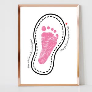 May include: A white framed picture with a pink baby footprint inside a black outline. The text "Papa, I'm following in your footsteps!" and "Step by step with lots of love!" is written in black cursive.