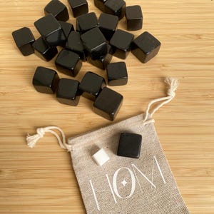 Puede incluir: Un juego de cubos de enfriamiento para whisky de piedra negra en una pequeña bolsa de lino con la palabra "HOM" impresa en ella. La bolsa también contiene un cubo de piedra blanca.
