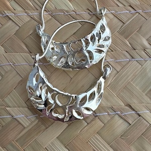 May include: A pair of silver hoop earrings with a delicate, leafy design. The earrings are made of a thin, wire-like material and have a crescent shape.