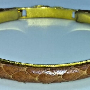 May include: A brown leather bracelet with a gold metal band. The leather has a snakeskin pattern.