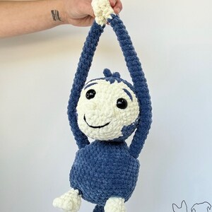 May include: A crocheted blue and white monkey toy with a smiling face. The monkey is hanging by its arms and has a long tail.