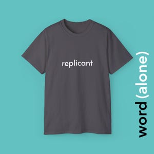 May include: A dark gray t-shirt with the word "replicant" printed in white across the chest. The shirt is displayed on a teal background. The words "word (alone)" are printed vertically on the right side of the image.