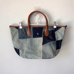 May include: A patchwork denim tote bag featuring various shades of blue fabric, including light-wash and dark indigo panels. The bag has two brown leather handles, a top leather trim, and a small white embroidered polo player logo on the front.