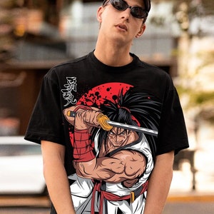 May include: Black t-shirt featuring a graphic of a samurai warrior holding a katana sword against a red sunburst background. The warrior is depicted in a dynamic pose, with long black hair and a determined expression. Japanese characters are printed on the upper left.