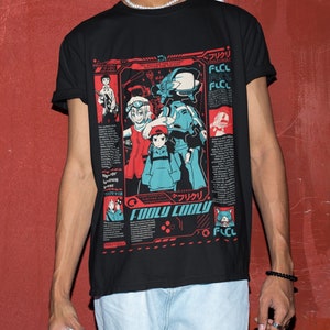 Puede incluir: Camiseta negra con un estampado gráfico de personajes de anime de la serie "FLCL" (Fooly Cooly). El gráfico incluye el texto "Fooly Cooly" y "フリクリ" en japonés.