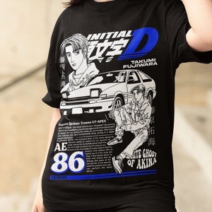 Peut inclure: T-shirt noir avec un imprimé graphique blanc d'une voiture, d'un pilote et du texte "Initial D Takumi Fujiwara AE86 Trueno".