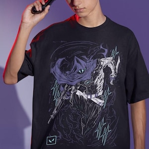 Peut inclure: T-shirt noir avec un imprimé graphique d'une figure cagoulée tenant une arme. La figure est entourée d'un nuage de fumée tourbillonnant. Le graphique est dans des tons de violet, bleu et blanc. Le t-shirt a un petit logo dans le coin inférieur gauche.