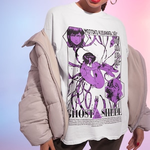 Peut inclure: T-shirt blanc avec un imprimé graphique violet et noir d'un personnage de l'anime "Ghost in the Shell". Le graphique comprend le texte "Motoko Kusanagi" et "攻殻機動隊".