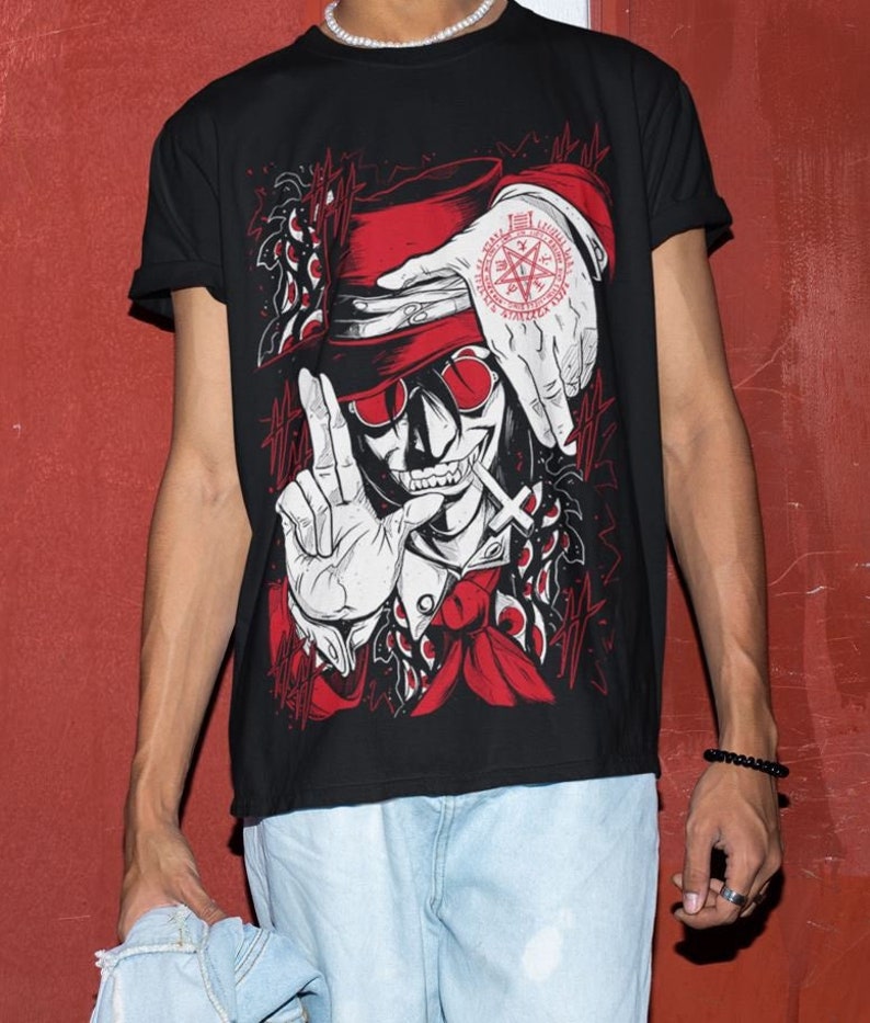 May include: Black t-shirt with a graphic print of a vampire with a red hat and a pentagram symbol. The vampire is wearing a red scarf and has a cross necklace.