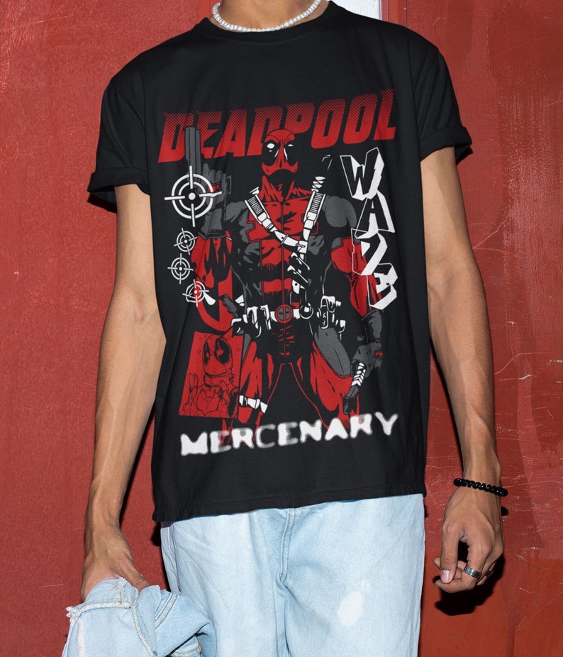 Puede incluir: Camiseta negra con una ilustraci&oacute;n roja y negra de Deadpool, un personaje de superh&eacute;roe, sosteniendo un arma. El texto "DEADPOOL" y "MERCENARY" est&aacute; impreso en la camiseta en blanco.
