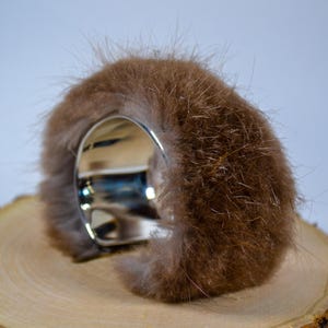 May include: A brown fur cuff bracelet with a wide, polished silver band. The fur is a warm, medium brown color and appears soft and textured. The bracelet is set on a wooden surface.