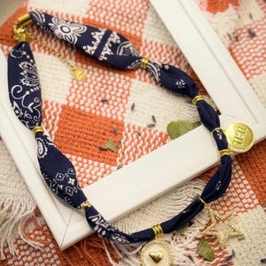 Peut inclure: Un collier en tissu bleu marine avec un motif cachemire blanc. Le collier comporte des accents et des breloques dorés, dont une étoile, un cœur et un disque avec le chiffre 11:11.