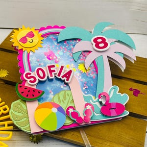 May include: A colorful birthday cake topper with a summer theme. It features a sun with sunglasses, a palm tree with the number 8, and the name "SOFIA". Other elements include a watermelon slice, beach ball, and flamingo.