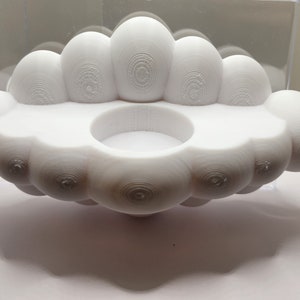May include: White ceramic candle holder shaped like a cloud with multiple rounded bumps. The holder has a circular depression in the center for a candle.