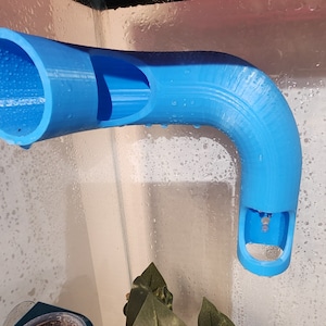 May include: A blue plastic 3D printed pipe with a curved section. The pipe has a hole on the side and a larger opening on the top.