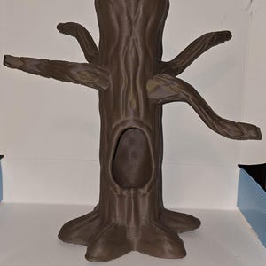 May include: A brown, tree-shaped decorative item with a hollowed-out trunk and several outstretched branches. The item has a textured surface, resembling tree bark, and is likely made of a durable material. The design includes a large opening in the trunk.