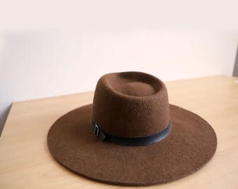 May include: A brown fedora hat with a wide brim and a black band. The hat is made of a felt-like material and has a classic design. The brim measures approximately 7.6 cm.