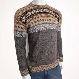 Puede incluir: Un suéter marrón y beige con un patrón geométrico. El suéter de cuello redondo presenta un diseño de diamantes y flechas en tonos marrón, beige y blanco. Las mangas largas y el dobladillo inferior tienen un borde estampado. Prenda cálida.