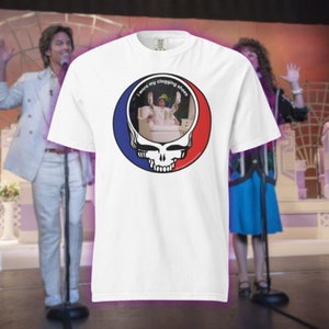 May include: White t-shirt featuring a graphic of a skull with a red and blue circle, and a picture of a person wearing white clothing and shoes. The text "I wore my clogging shoes" is above the picture.