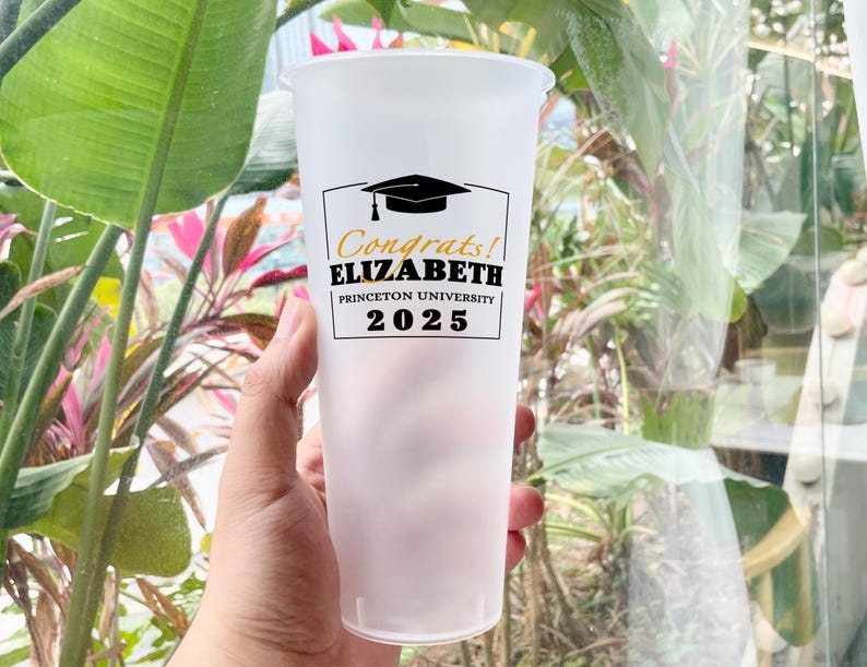 May include: A clear plastic cup with a black and gold graduation design. The text on the cup reads "Congrats! Elizabeth Princeton University 2025".