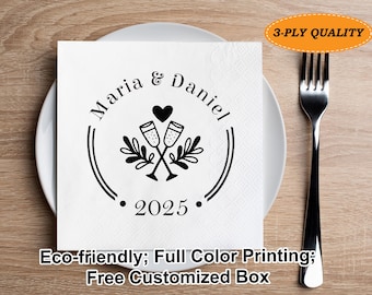 Può includere: Tovagliolo quadrato bianco con un disegno circolare nero con i nomi "Maria & Daniel", due calici di champagne, un cuore e l'anno "2025". Il tovagliolo è su un piatto bianco con una forchetta.