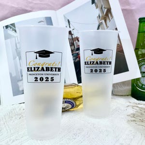 May include: Two white plastic cups with black and gold text. The text on the cups reads "Congrats! ELIZABETH PRINCETON UNIVERSITY 2025".