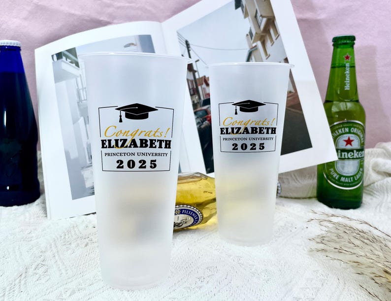 May include: Two white plastic cups with black and gold text. The text on the cups reads "Congrats! ELIZABETH PRINCETON UNIVERSITY 2025".