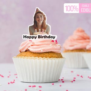 May include: A cupcake with pink frosting and a decorative edible topper that says "Happy Birthday". The topper features a photo of a person holding a cake with candles. The image also includes the text "100% Edible Topper Edible Ink".