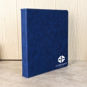 May include: A blue leather binder with a white logo that says "COMPANY SLOGAN" and a white geometric design.