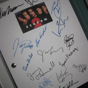 Könnte beinhalten: Ein weißes Papier mit mehreren Unterschriften in blauer und schwarzer Tinte. Ein kleines Bild des Films "Scream 2" befindet sich in der Mitte. Die Unterschriften scheinen Autogramme zu sein.