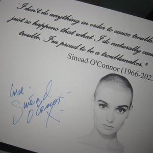 May include: A print featuring a portrait of Sinéad O'Connor with a quote: "I don't do anything in order to cause trouble. It just so happens that what I do naturally causes trouble. I'm proud to be a troublemaker." Includes her signature.