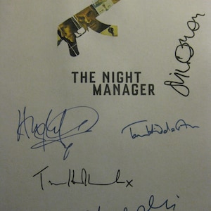 May include: A white poster with the title "THE NIGHT MANAGER" in black block letters. Above the title is an image of an AK-47 rifle, with the gun's outline filled with images of faces. Several signatures are written in blue ink.