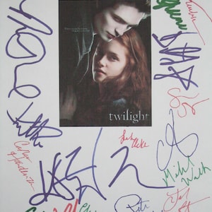 May include: A framed image of the "Twilight" movie poster, encircled by multiple signatures in various colours. The poster features two people and the word "twilight" in white. The signatures are in different colours.